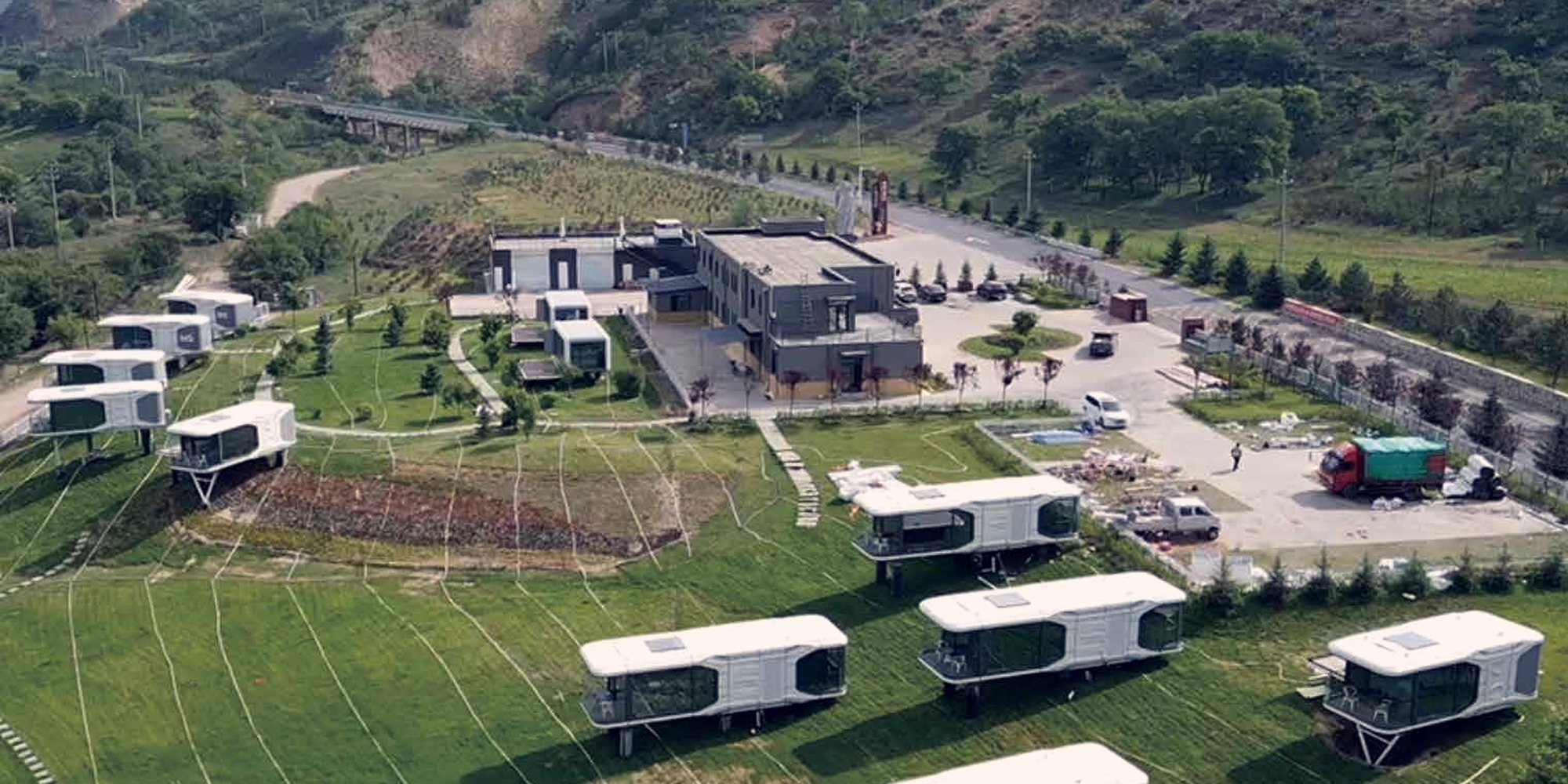 Aerial view of a capsule glamping camp laid out across a green valley